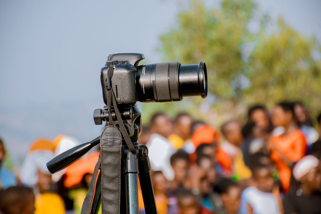Camera on a tripod capturing people at an outdoor event in Ruhango, Rwanda.